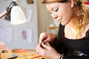 Young Woman Making Jewelry At Home With Lamp